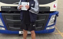 Marcin proudly holding his HGV test certificate in front of a Volvo articulated training vehicle at MT Training Services Newbury