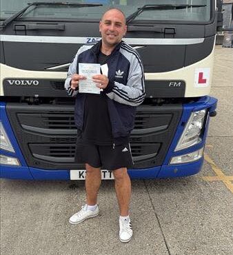 Marcin proudly holding his HGV test certificate in front of a Volvo articulated training vehicle at MT Training Services Newbury