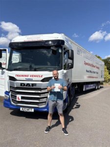 Michael holding his CE 3b pass certificate in front of an articulated MT Training vehicle at the Tortworth training centre in South Gloucestershire