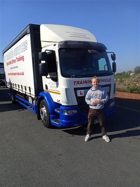 Trainee driver standing in front of a Cat C training lorry at MT Training Services Taunton after passing HGV test on a clear day
