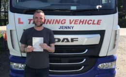Male trainee driver holding pass certificate in front of CE training lorry after passing 3a test at MT Training Services Kidderminster