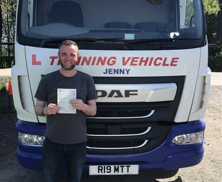 Male trainee driver holding pass certificate in front of CE training lorry after passing 3a test at MT Training Services Kidderminster