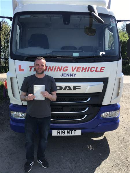 Male trainee driver holding pass certificate in front of CE training lorry after passing 3a test at MT Training Services Kidderminster