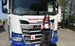 Female trainee driver holding pass certificate in front of CE training lorry at MT Training Services Tortworth
