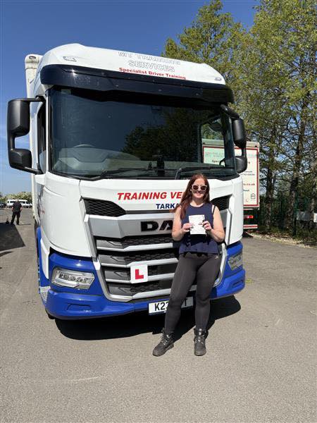 Female trainee driver holding pass certificate in front of CE training lorry at MT Training Services Tortworth